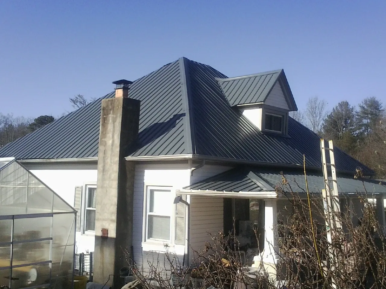 Dark blue standing seam metal roof on a white farmhouse with dormer — Slate & Tile Roof Repair by Roofing Brothers in Otter Creek