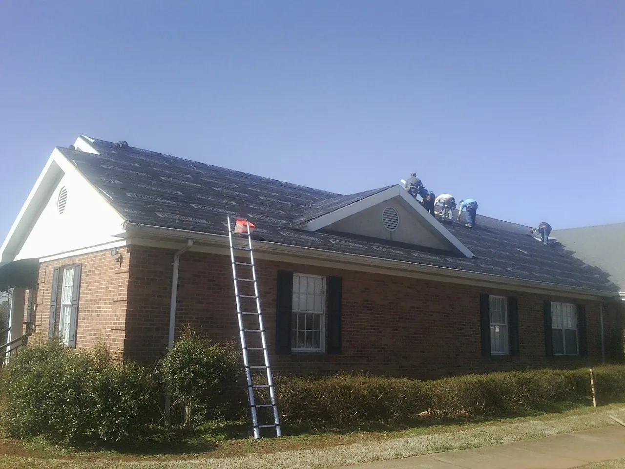 Crew tearing shingles off a brick ranch roof with a ladder set — Emergency Roof Repair work by our crew in Otter Creek