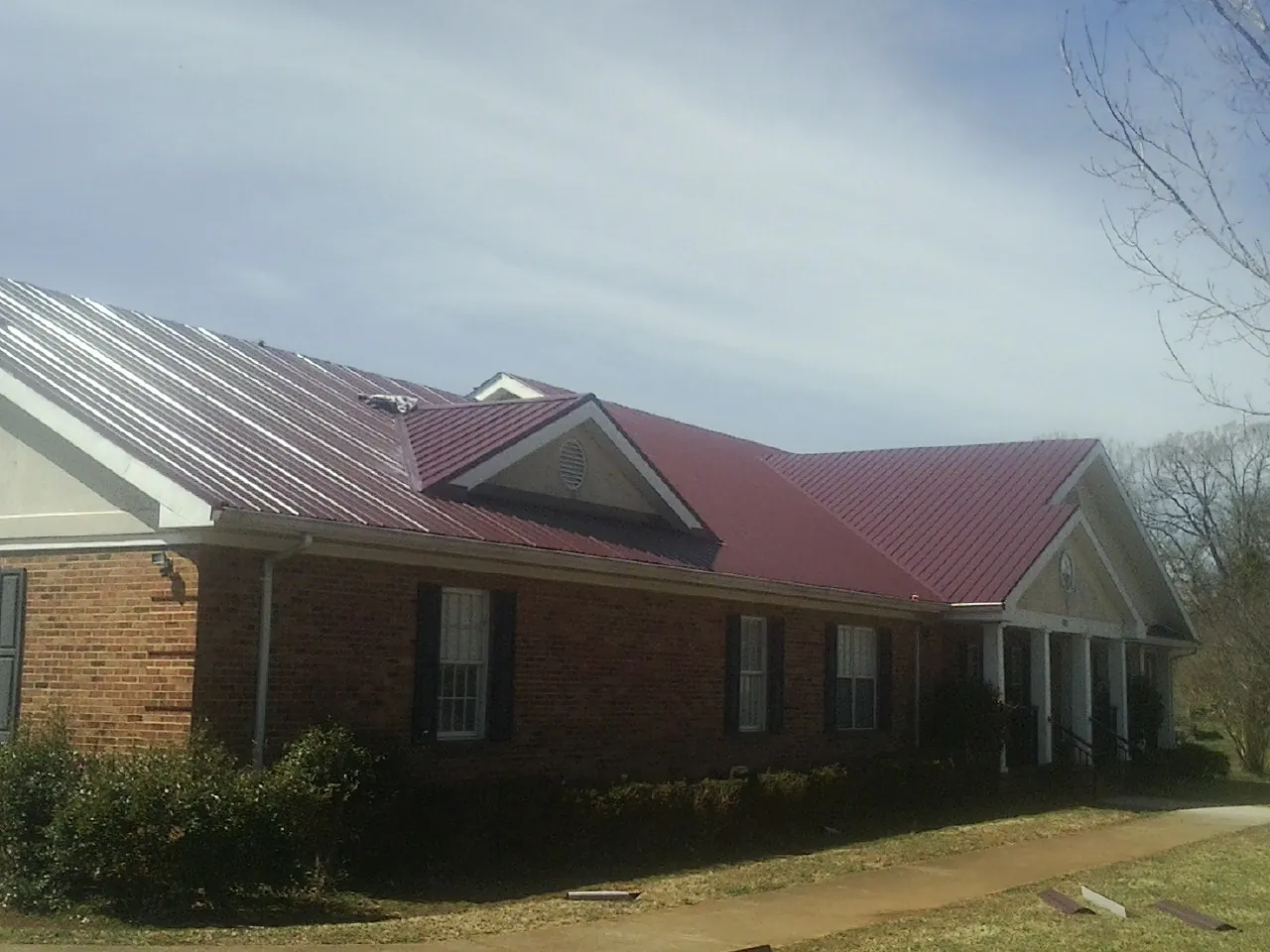 Red metal roof with gabled entries on a long brick building, from a Hail Damage Roof Repair job in Otter Creek
