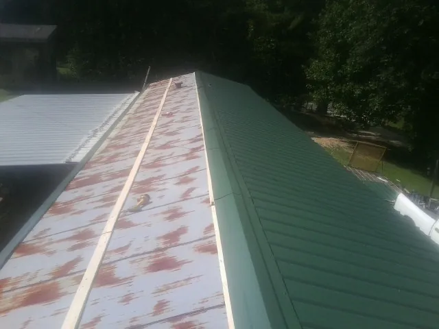 Old rusted panels beside newly installed green metal roofing — Wind Damage Roof Repair by Roofing Brothers in Otter Creek