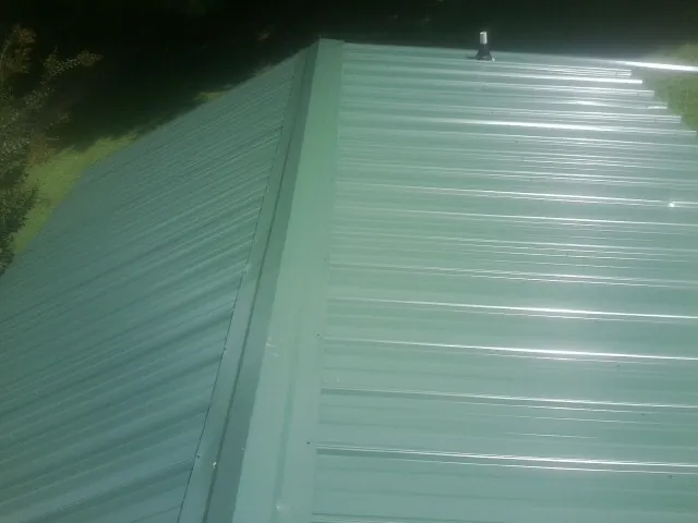 New green metal panels meeting at the ridge of a roof — Flat Roof Repair work by our crew in Otter Creek