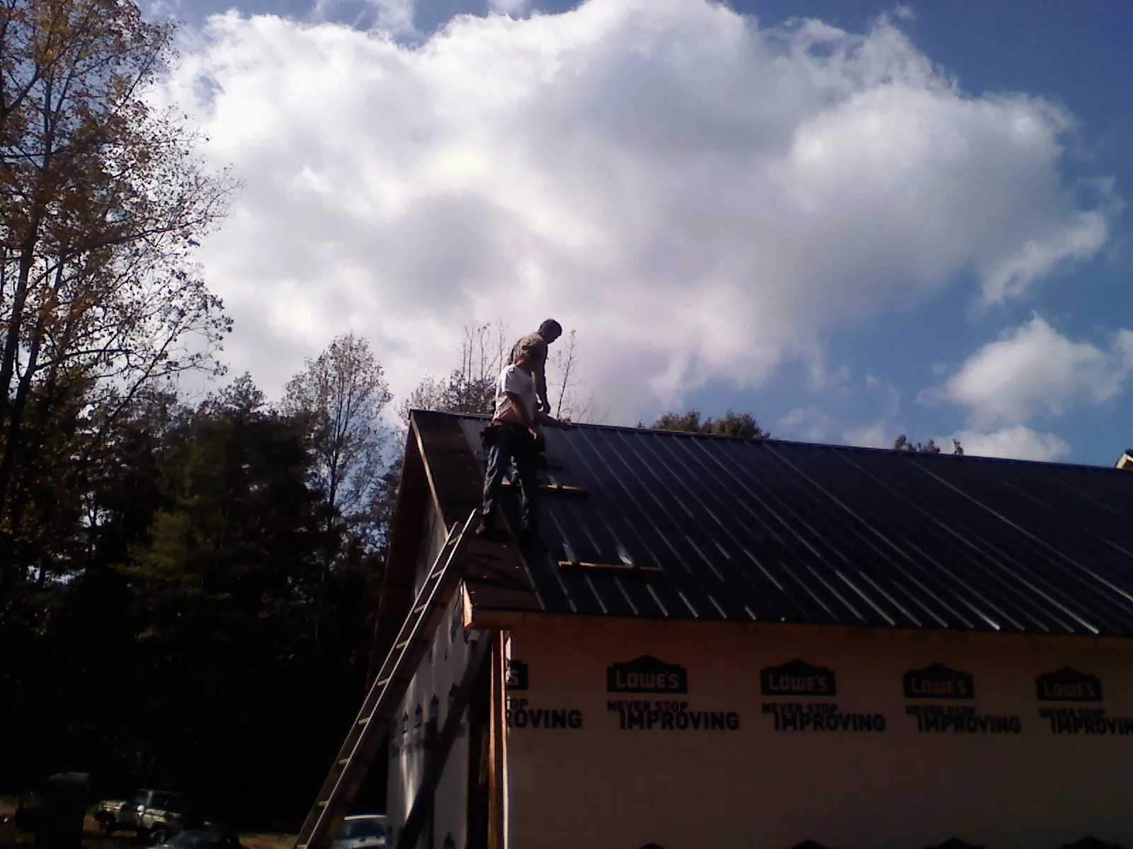 Roofer fastening dark metal panels high against a cloudy sky, from a Roof Inspection job in Otter Creek