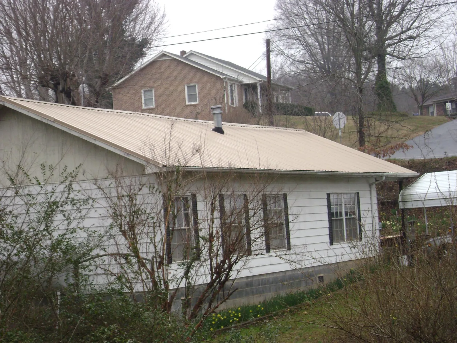 Tan metal roof on a white sided house set into a hillside — Commercial Roofing by Roofing Brothers in Otter Creek