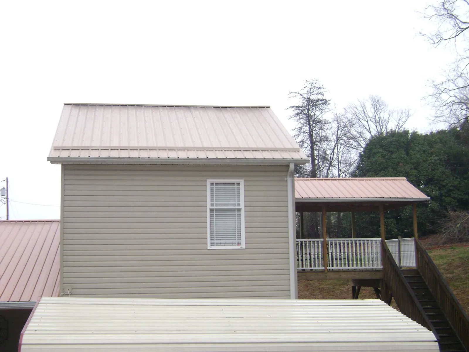 Tan metal roofs on a two story addition and attached porch, from a Roof Replacement job in Otter Creek